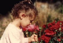 Small girl sniffing red poppy flowers